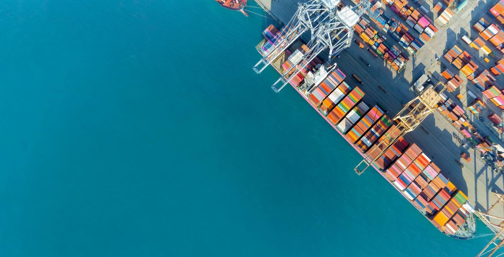 A bird's eye view of a freighter fully loaded with containers, blue sea and container harbour