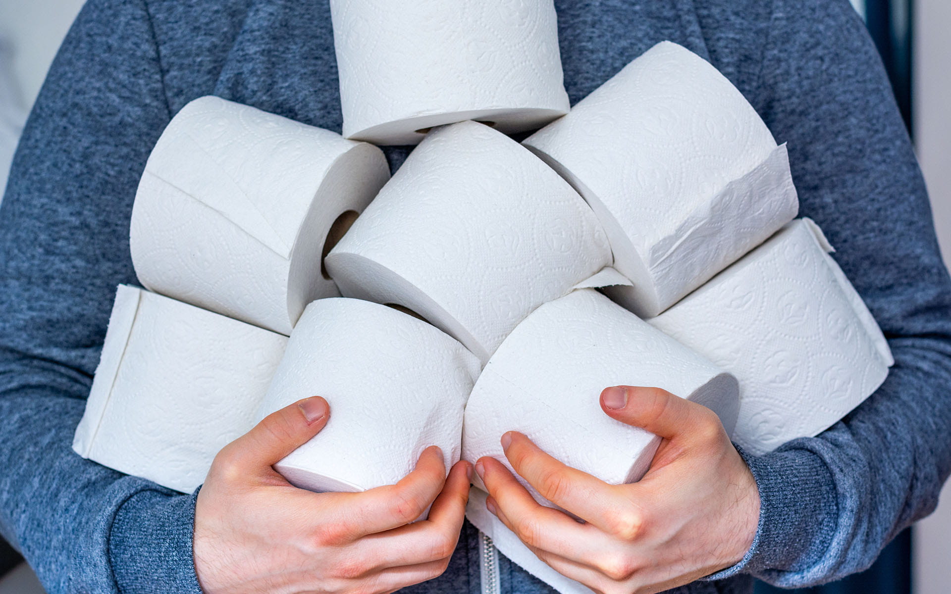 Person holding an armful of toilet paper rolls.