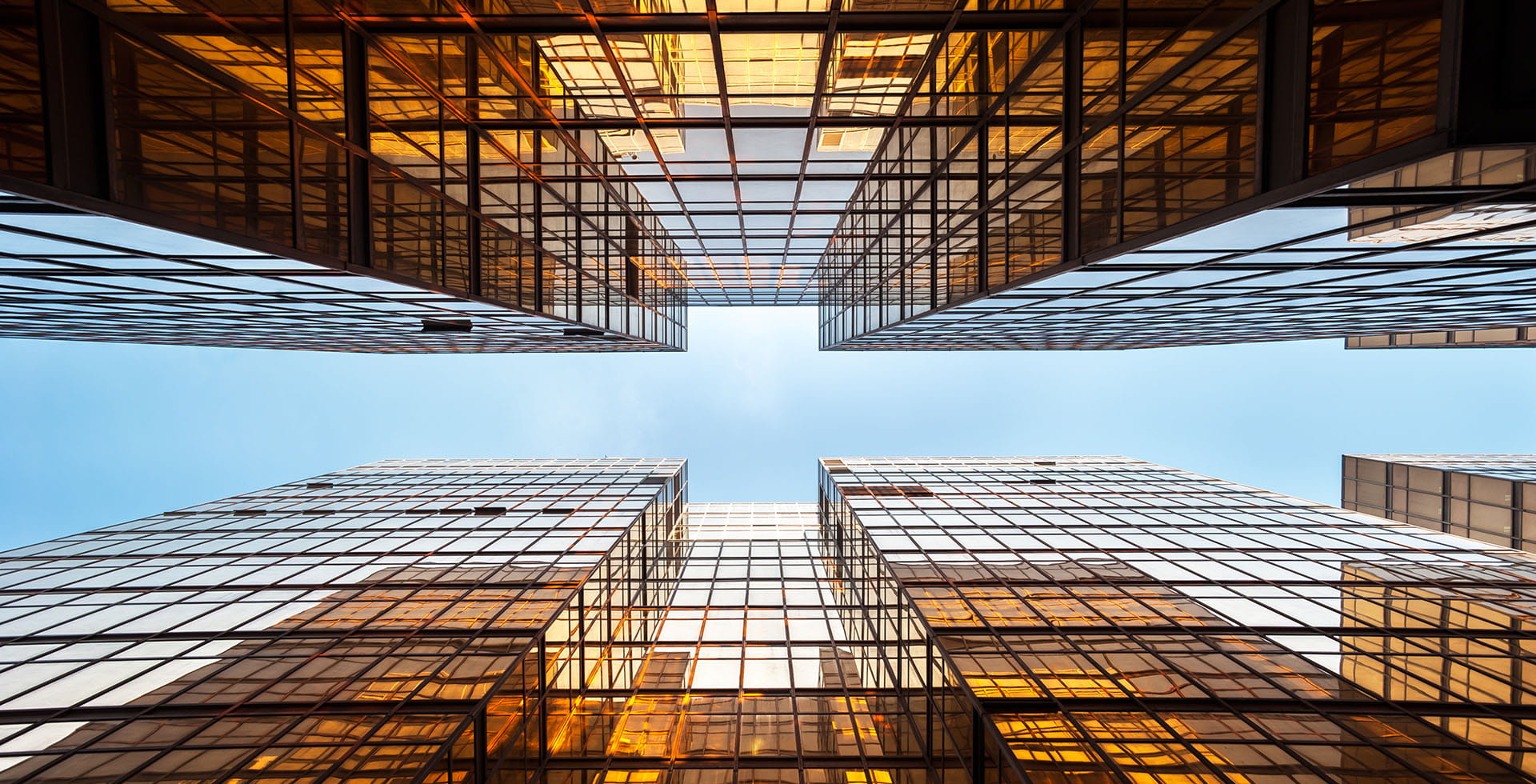 View looking up between glass skyscrapers reflecting golden light.